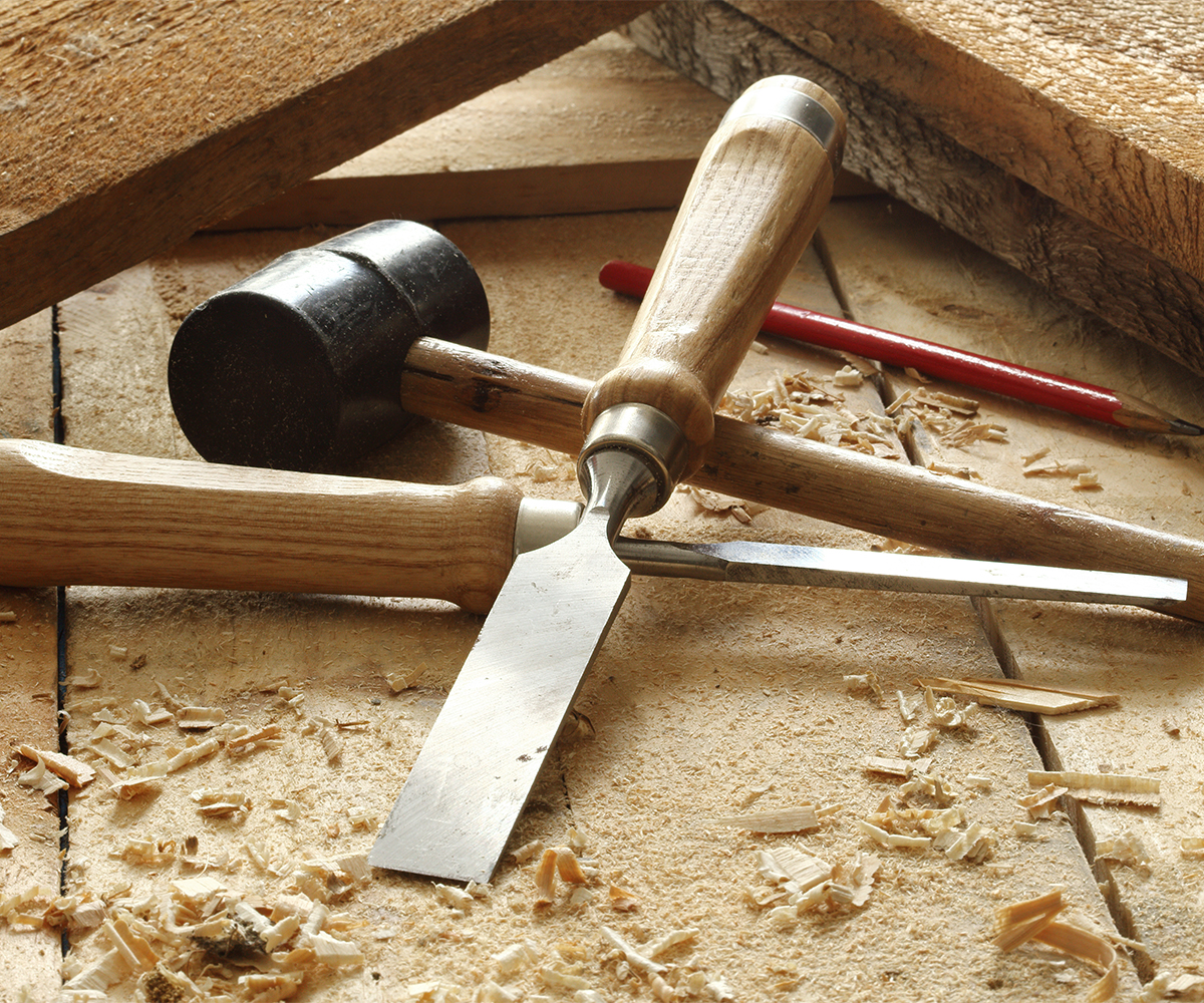 Wood chisels, mallet, and pencil on workbench covered in wood shavings.