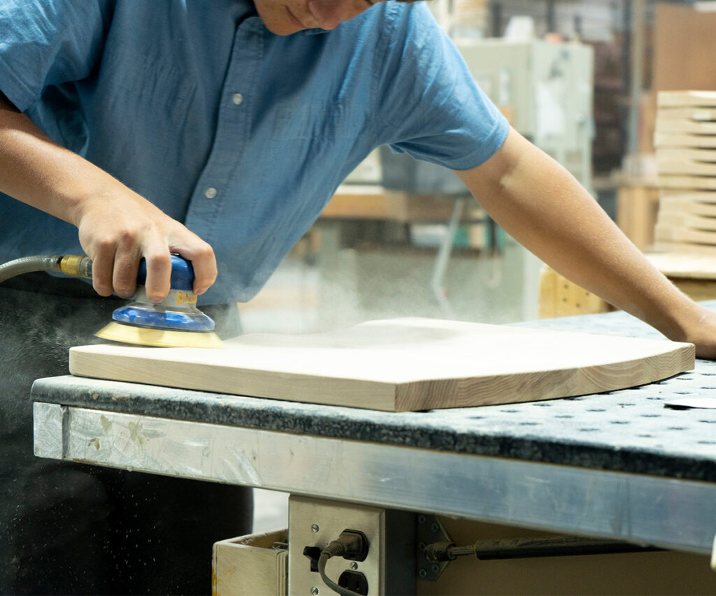 Amish woodshop builders sanding solid wood furniture by hand.