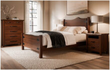 Bedroom with wooden Amish furniture, including a bed, nightstand, and tall dresser, with neutral bedding and decor.