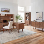 Mid-century modern office setup featuring Amish furniture, a large desk with a hutch, a white upholstered chair, a bookshelf, a sideboard, and decorative plants.