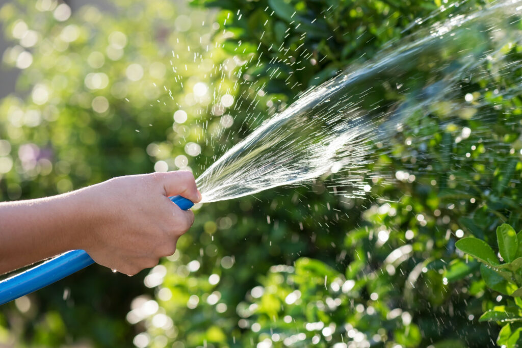 Hand rinsing outdoor furniture with a garden hose in a sunlit yard.