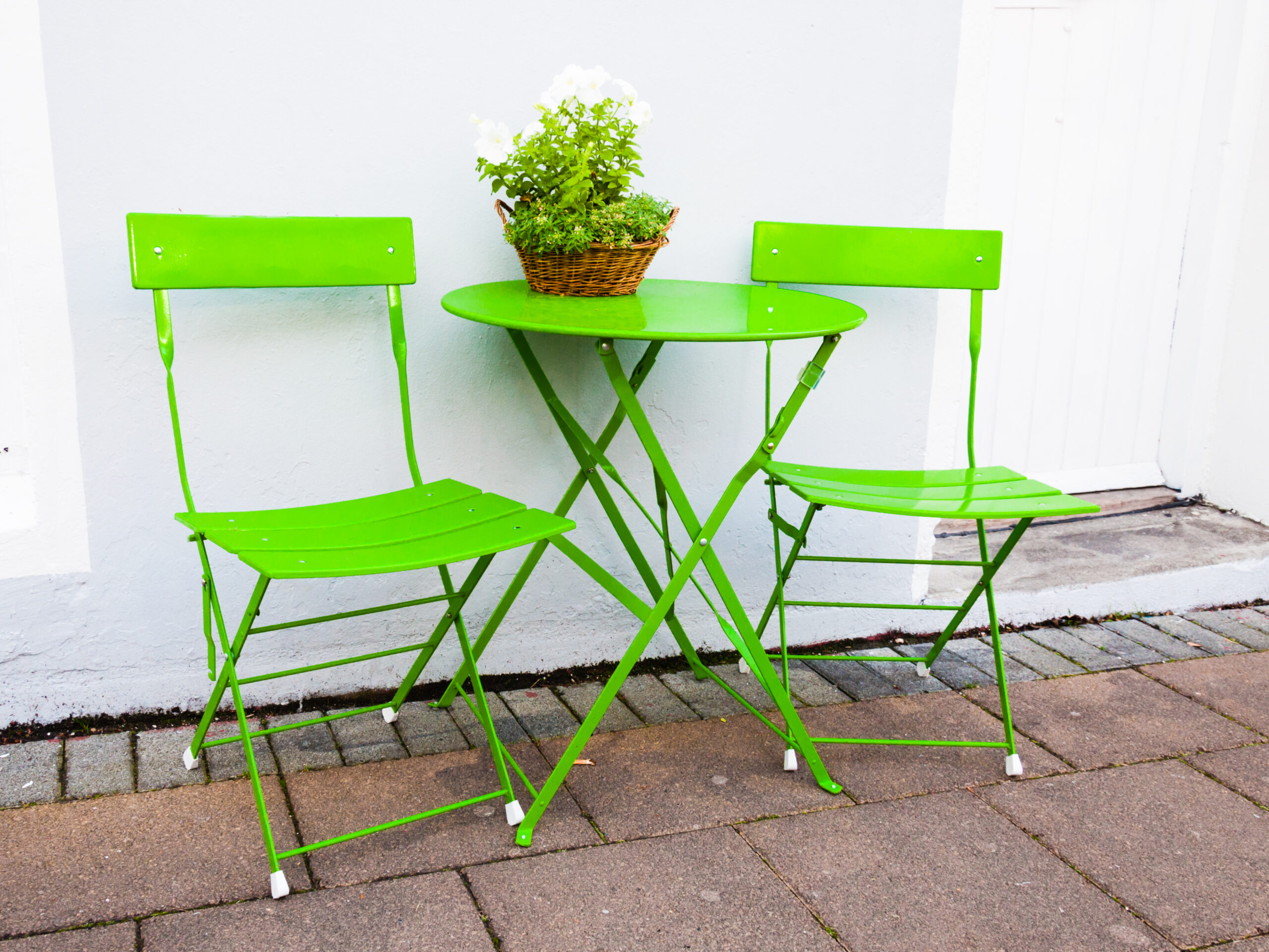 Bright green cheap bistro table with two chairs and potted plant on a patio.