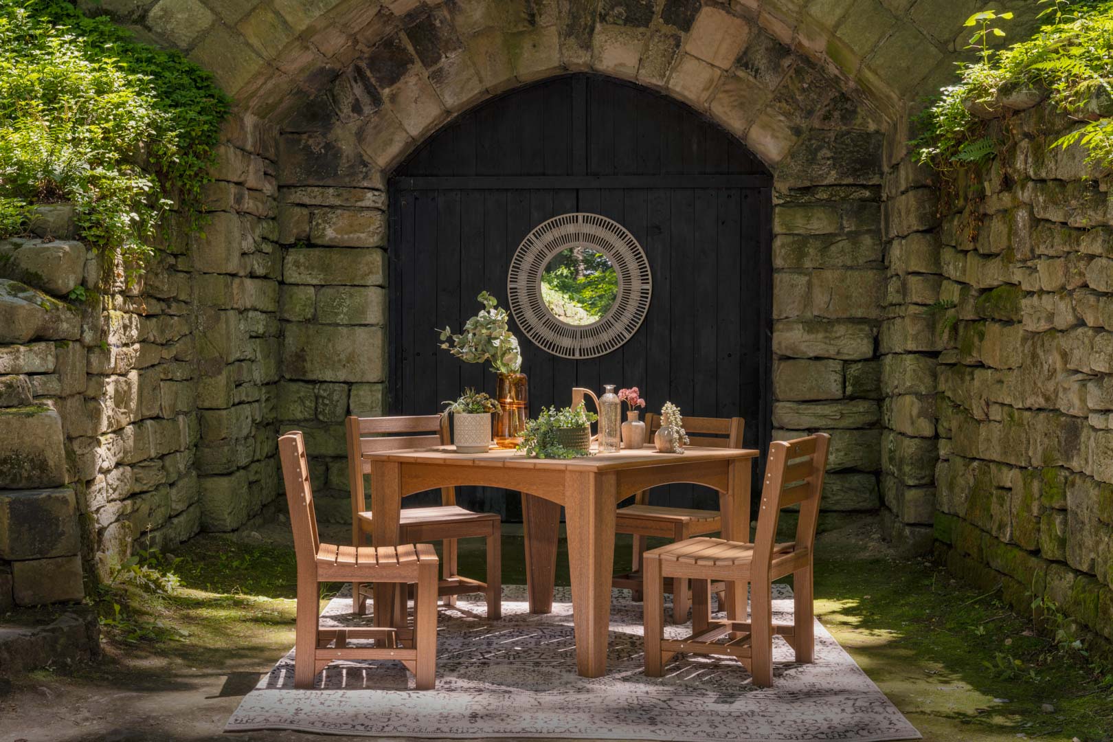 Poly outdoor dining set under a stone arch in a lush garden courtyard.