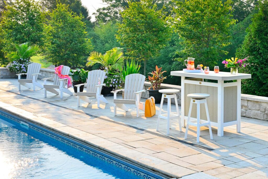 White poly Adirondack chairs and bar set arranged beside a backyard swimming pool.