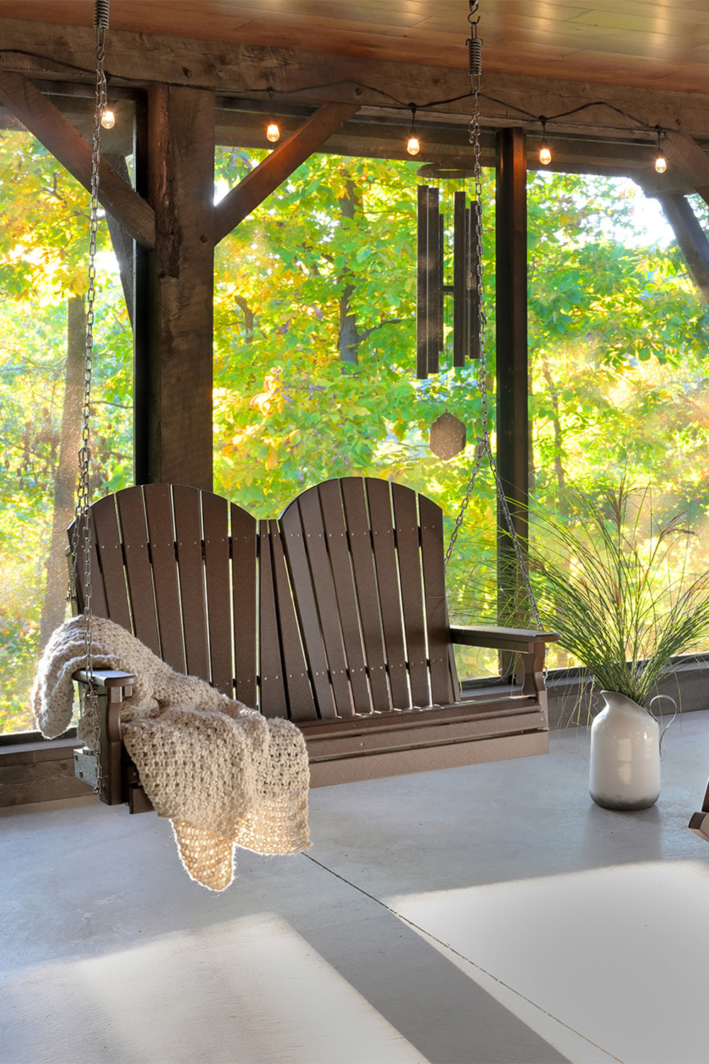 Brown poly Adirondack porch swing for two with knit throw on a covered patio.