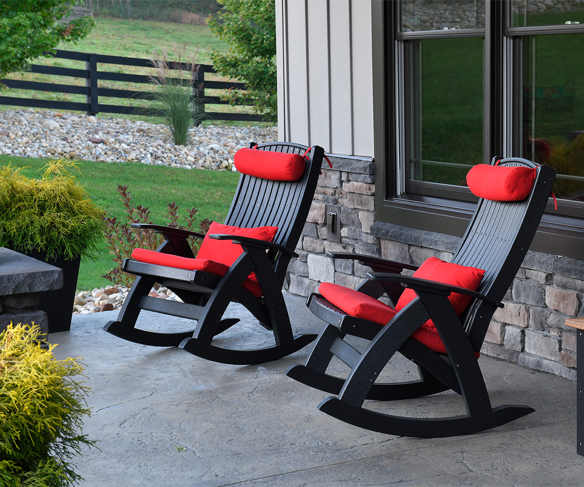 Two black poly rocking chairs with red cushions on a stone porch.
