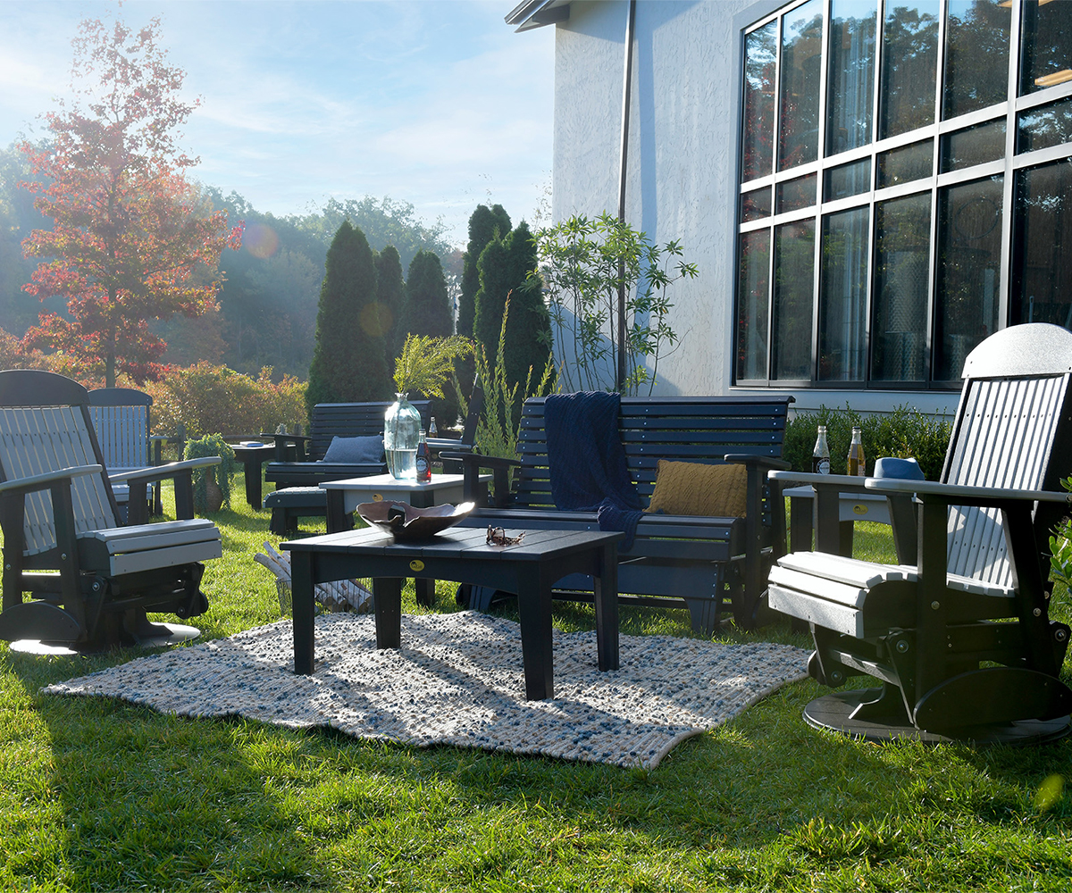 Mixed poly patio set—glider chairs, bench, coffee table—on lawn with rug and pillows.