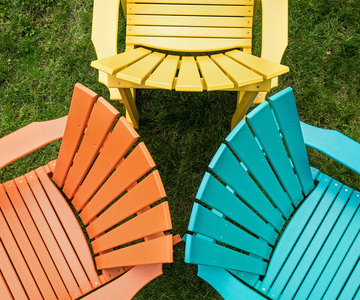 Yellow, orange, and teal poly Adirondack chairs viewed from above on grass.