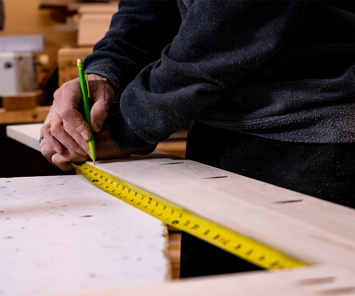 Close-up of a craftsman marking wood with a pencil and tape measure, showcasing the precision of Amish furniture makers.