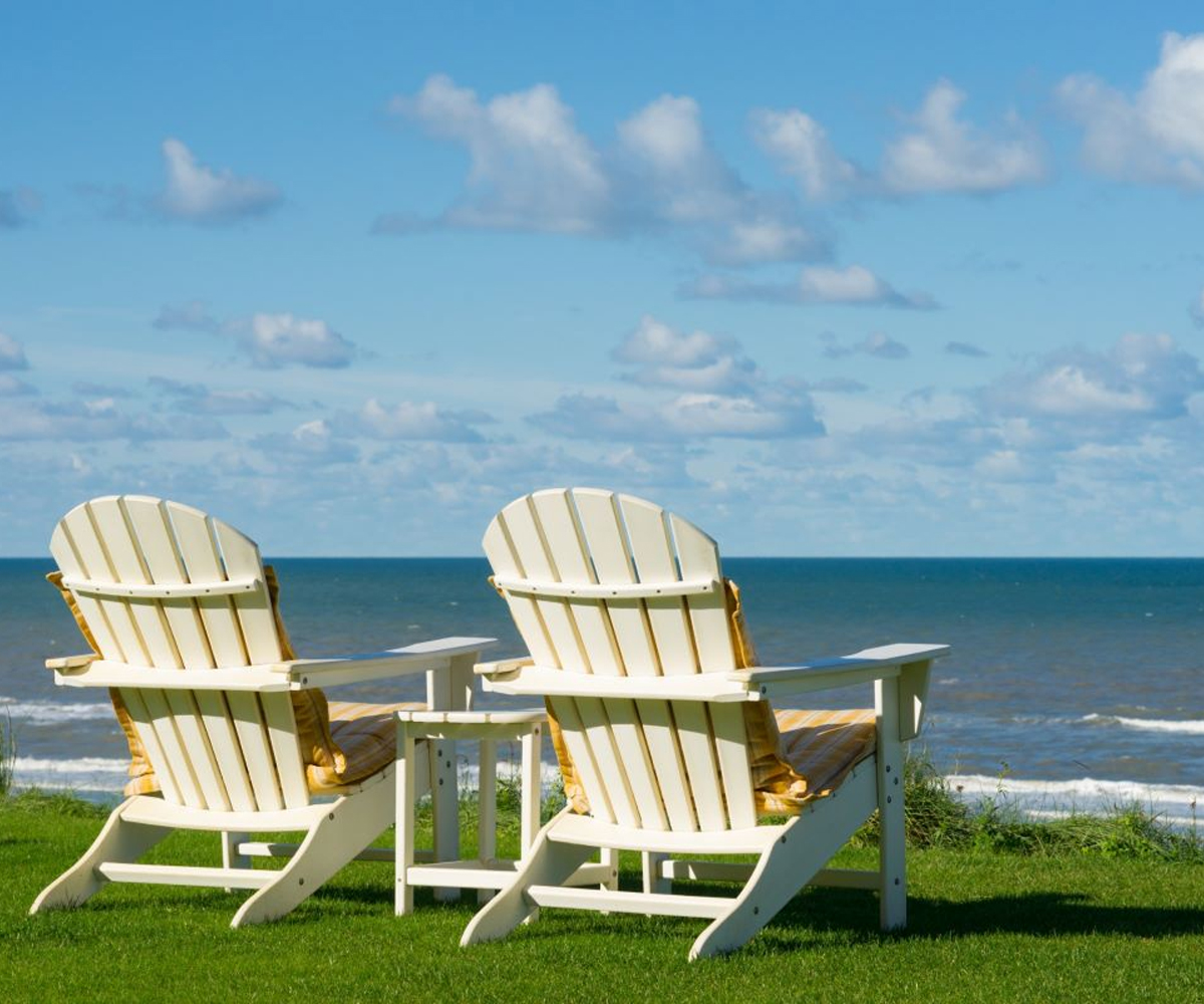 Adirondack chairs facing the ocean on a grassy lawn.