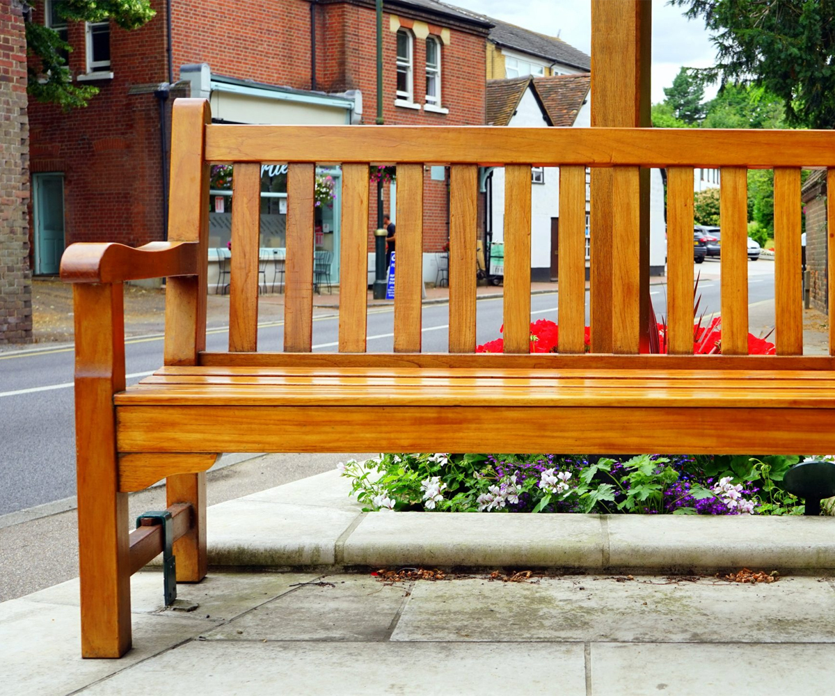 Wooden outdoor bench with slatted backrest on a sidewalk.