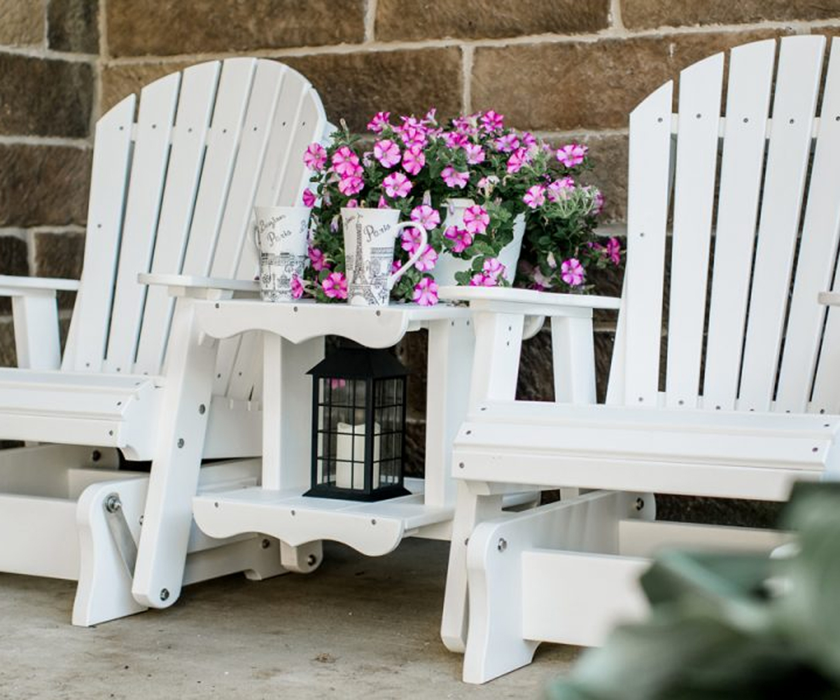 White Adirondack-style glider chairs with table and flowers.